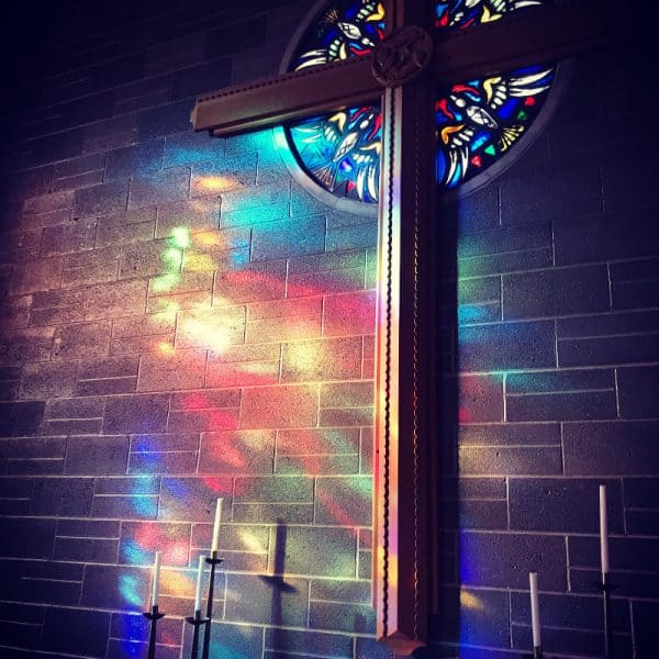Close up of our chapel cross with stained glass window colors bouncing off wall