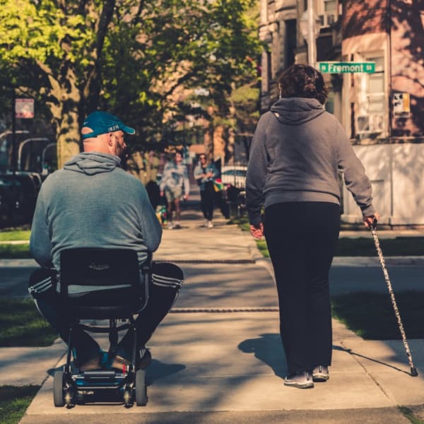 An elderly couple with one in a wheelchair and one with a walking cane