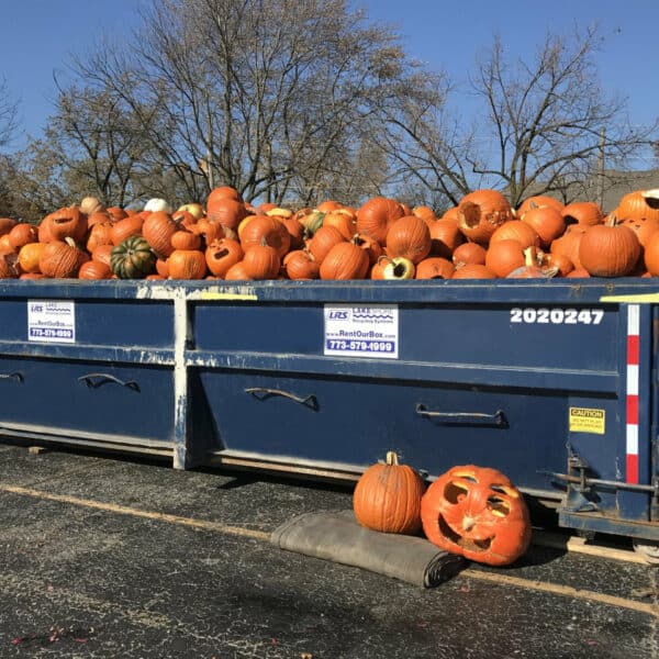 A garbage dumpster full of old Jack-o-lanterns